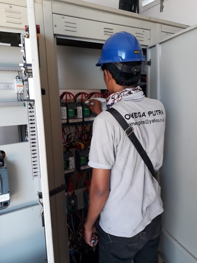 Teknisi berseragam Omega Putra bekerja pada panel listrik